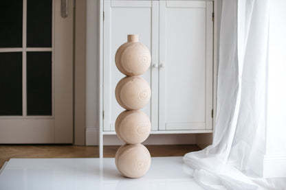 A handmade wooden furniture leg with four spheres, crafted from unfinished wood, displayed in an indoor setting.