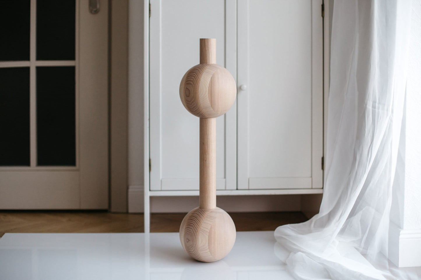 A handmade wooden furniture leg with two spheres, crafted from unfinished raw wood, displayed in an indoor setting.
