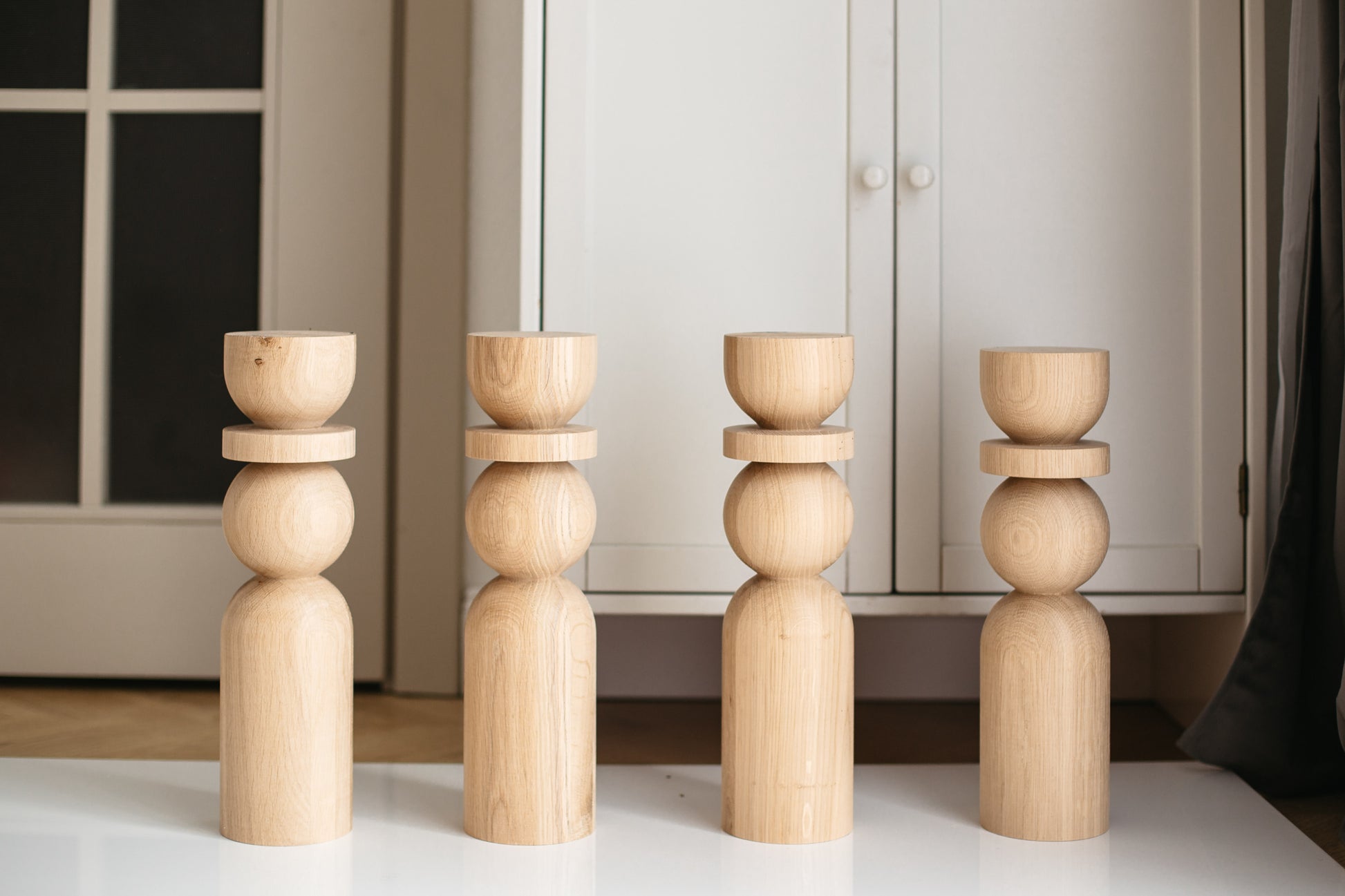 Four wooden candle holders of different heights arranged on a surface with a neutral background.